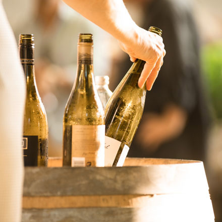 A wine bottle being picked up from a top of a barrel.