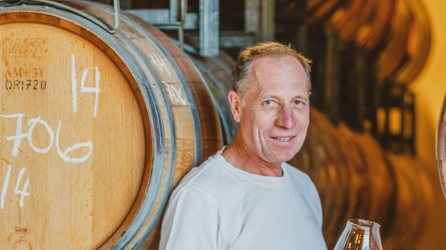 Rudi Bauer standing by wine barrels