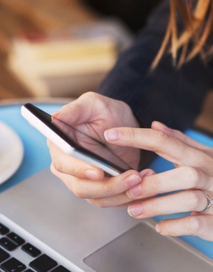 A woman using a smartphone with a coffee next to her.