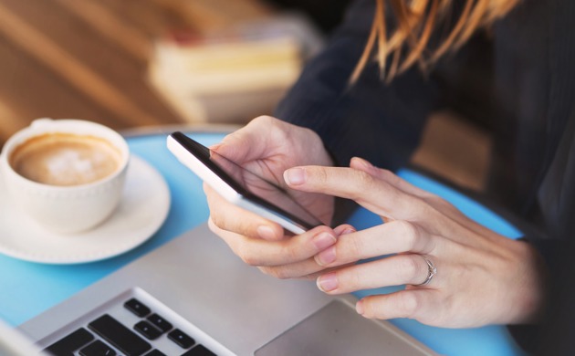 A woman using a smartphone with a coffee next to her.