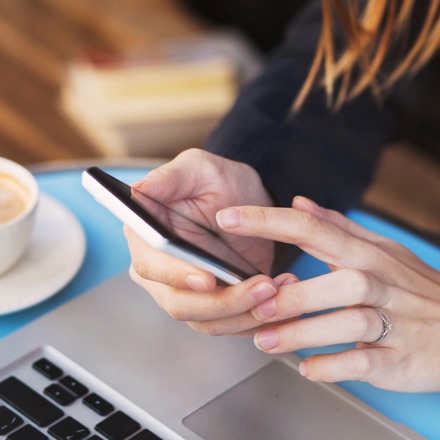 A woman using a smartphone with a coffee next to her.